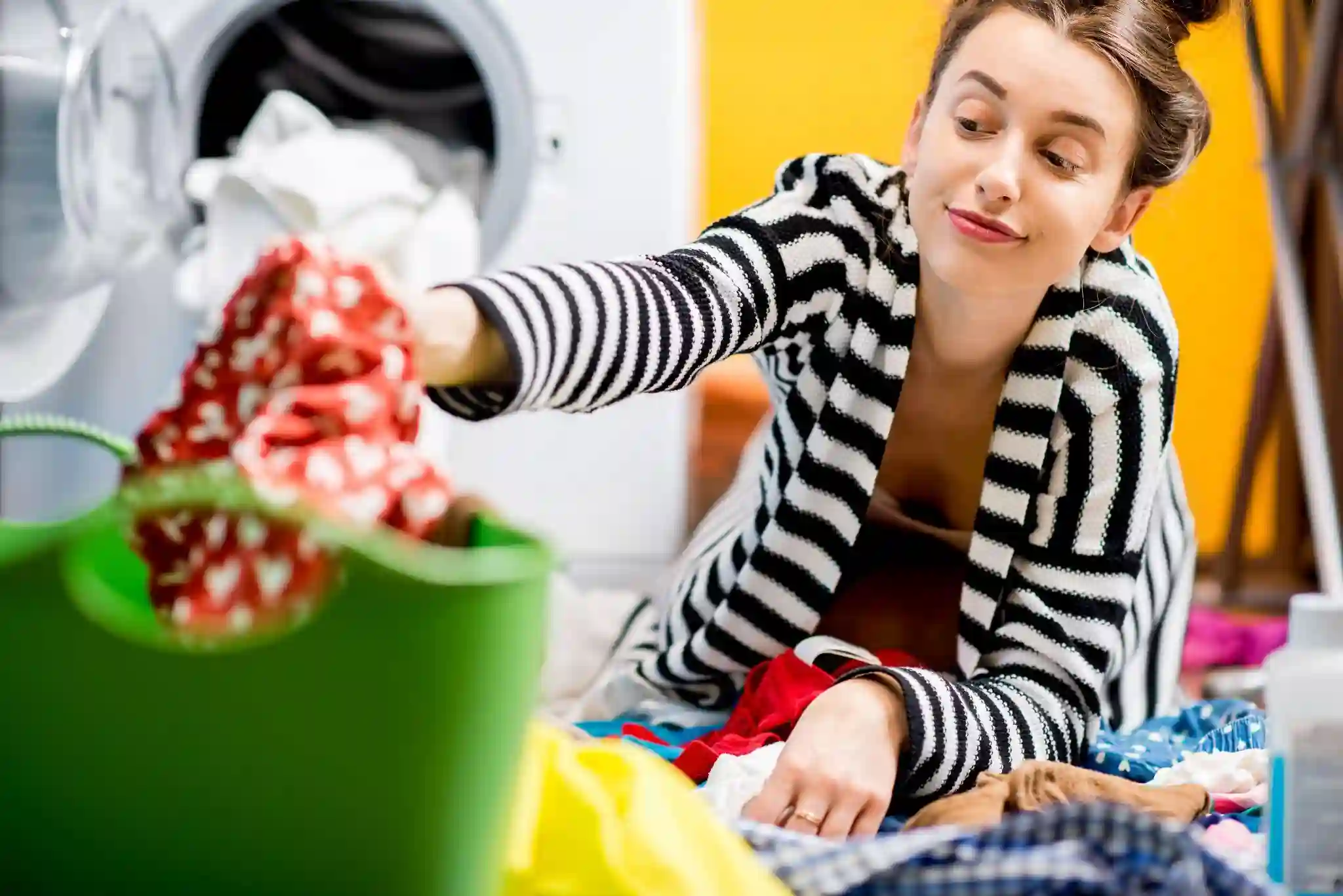 Woman sorting colored laundry sitting by the washing machine in a laundry room.