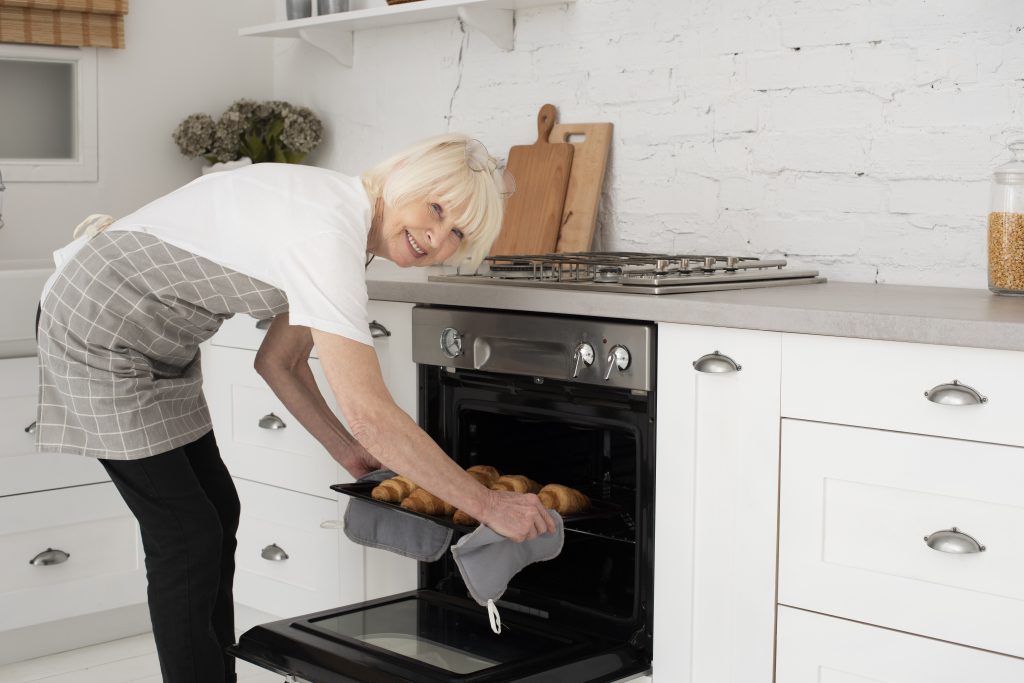 smiley-old-woman-holding-tray-with-croissants-oven