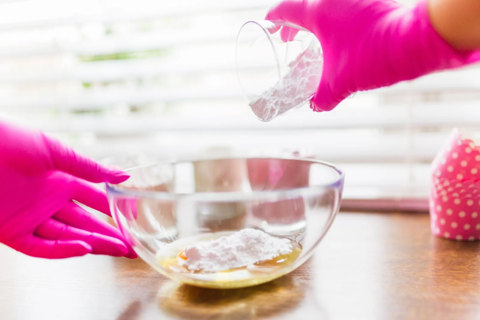 Hands wearing pink protective gloves mixing white power with liquid in a bowl